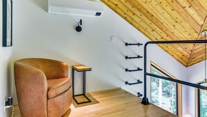 A room with a brown leather chair, a small wooden table, a white air conditioning unit, a black hanging light fixture, and a wooden ceiling. - Modern PNW Cabin on 10 Wooded Acres (Warren)