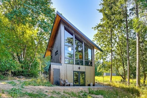 Uma cabana moderna com fachada de vidro ampla, cercada por uma floresta.
