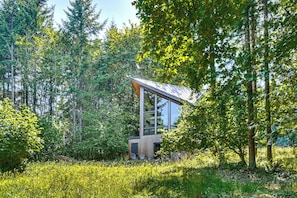 A modern cabin with a large glass window, surrounded by dense forest. - Modern PNW Cabin on 10 Wooded Acres (Warren)