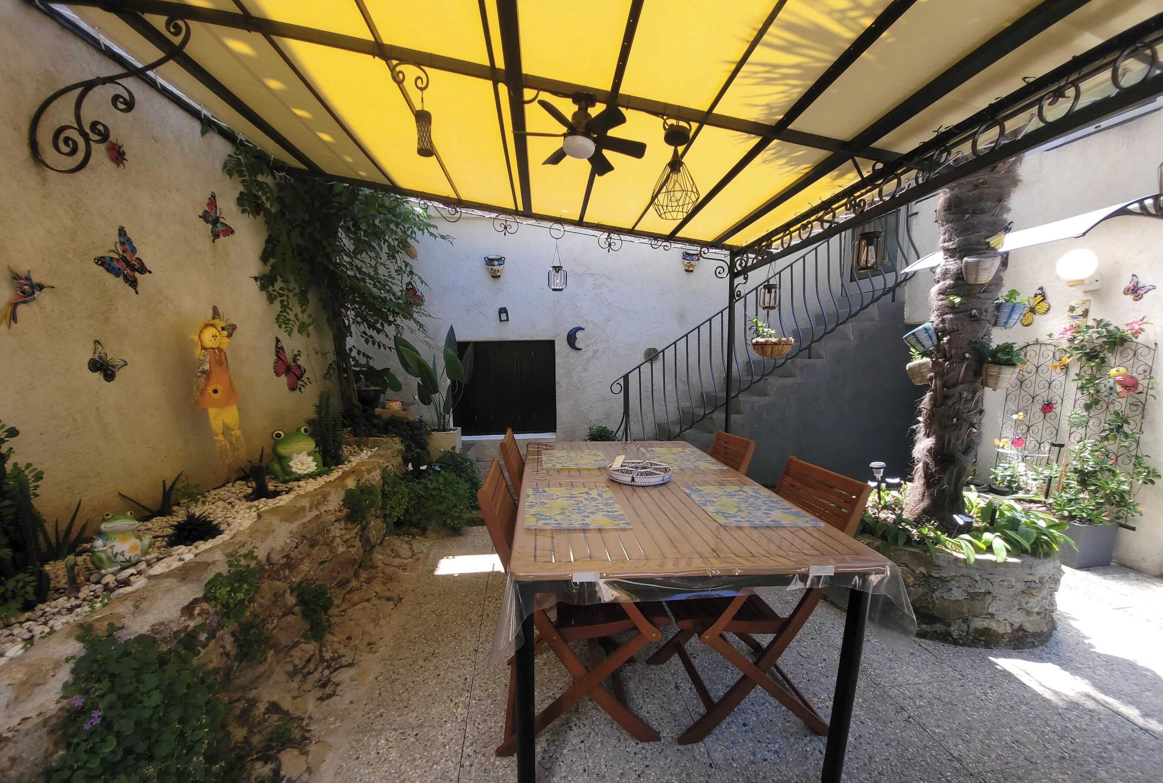 A covered patio with a table and chairs, surrounded by potted plants and decorative items.