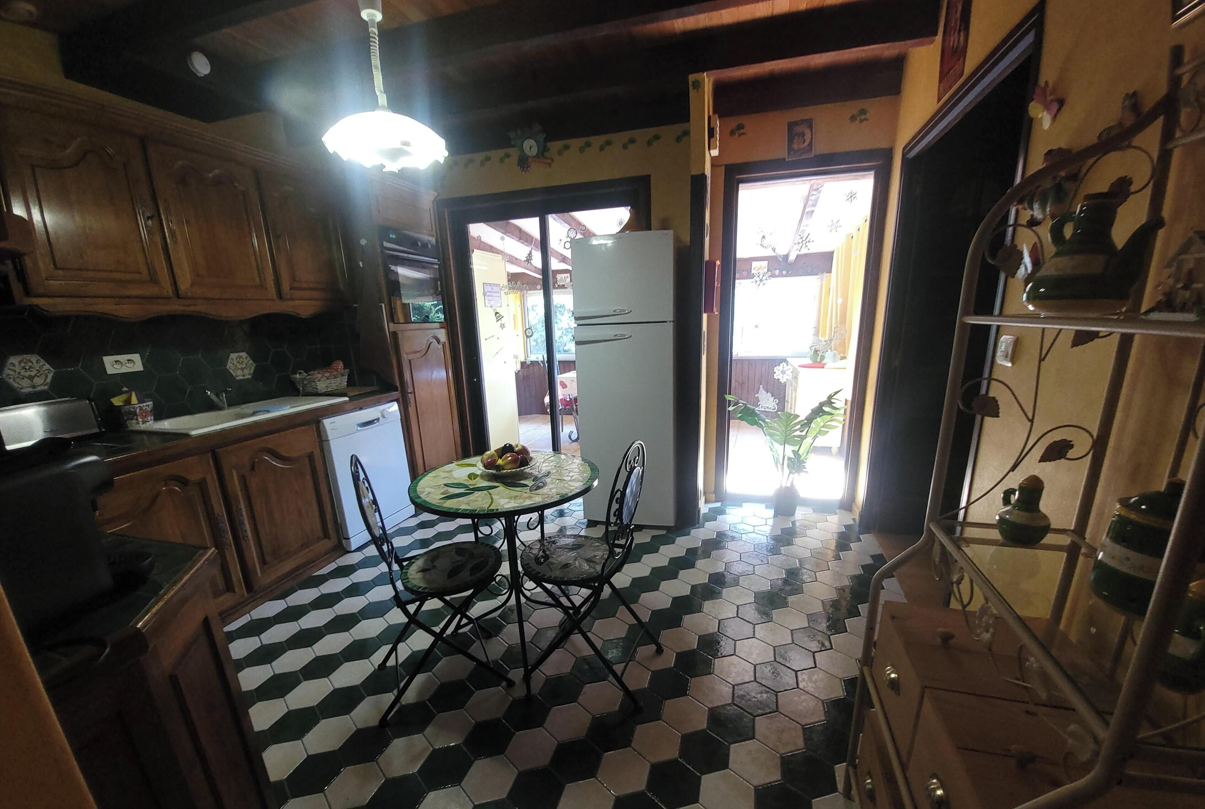 A kitchen with wooden cabinets, a white refrigerator, a dining table with chairs, and a tiled floor.