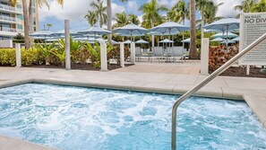 Ein Poolbereich mit Liegestühlen und Sonnenschirmen, umgeben von Palmen und einem Schild mit Spa-Regeln.