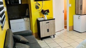 A living room with a sofa, a television mounted on the wall, a small cabinet, and a refrigerator. - Room-acama Guest House 455 Long rd, Welk (Matjhabeng)