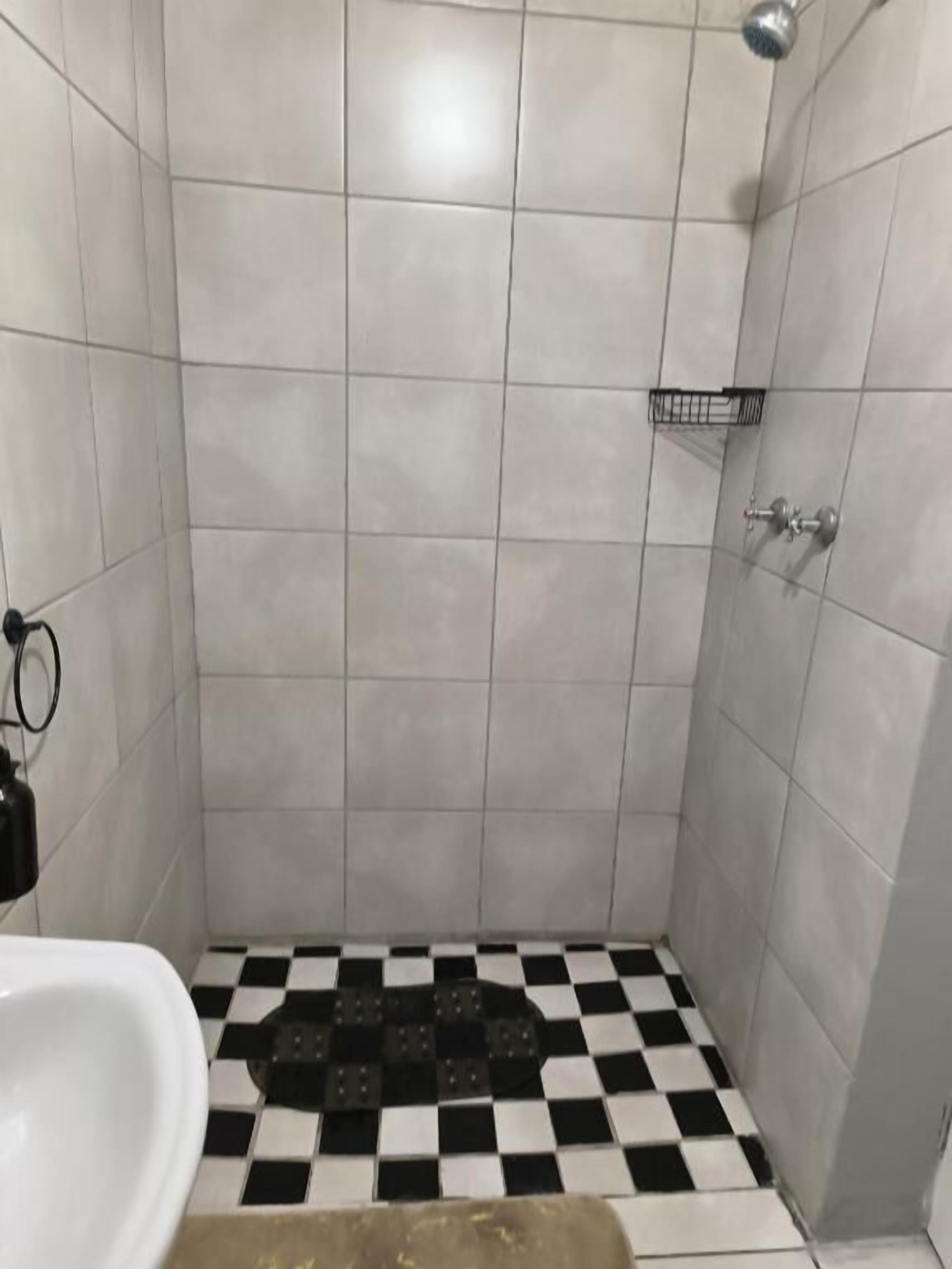 A bathroom with white tiled walls, a black and white checkered floor, a white sink, and a shower area.