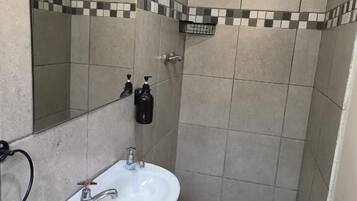Ein Badezimmer mit weißem Waschbecken, einem Spiegel und einer Duschkabine.