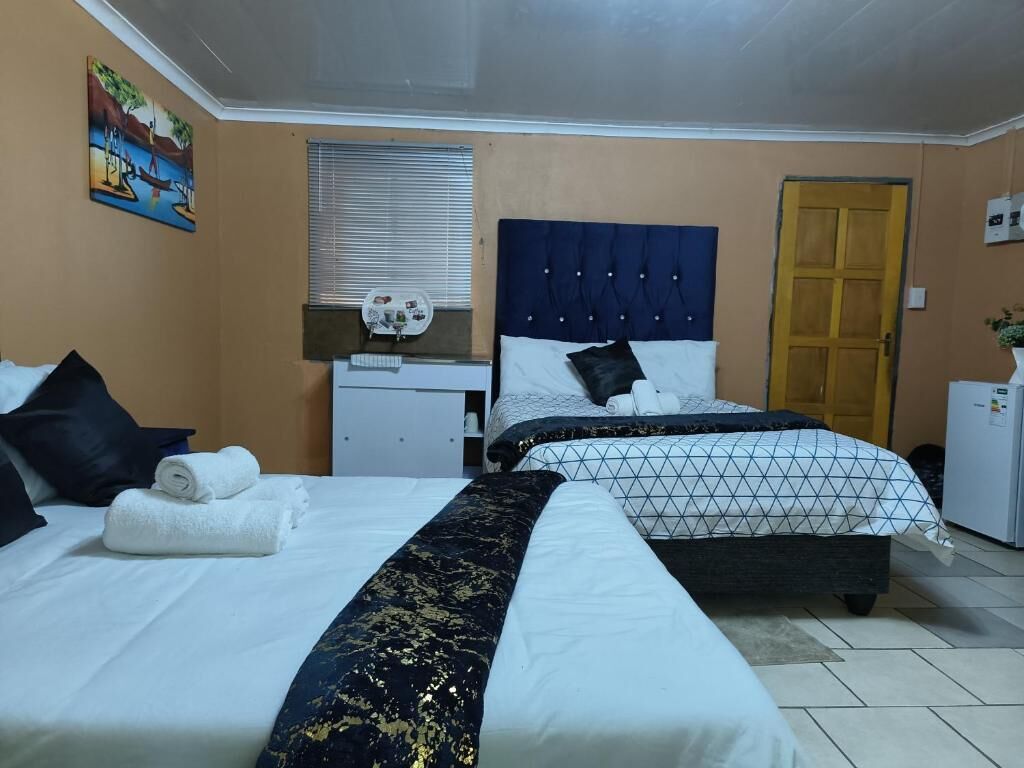 A hotel room with two beds, a desk, a window with blinds, and a door.