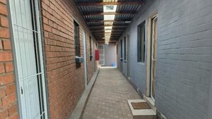 A corridor with brick walls, metal doors, and a tiled floor. - Room-acama Guest House 455 Long rd, Welk (Matjhabeng)