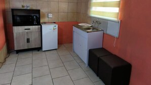 A compact kitchen with a microwave, refrigerator, sink, and a small bench. - Room-acama Guest House 455 Long rd, Welk (Matjhabeng)