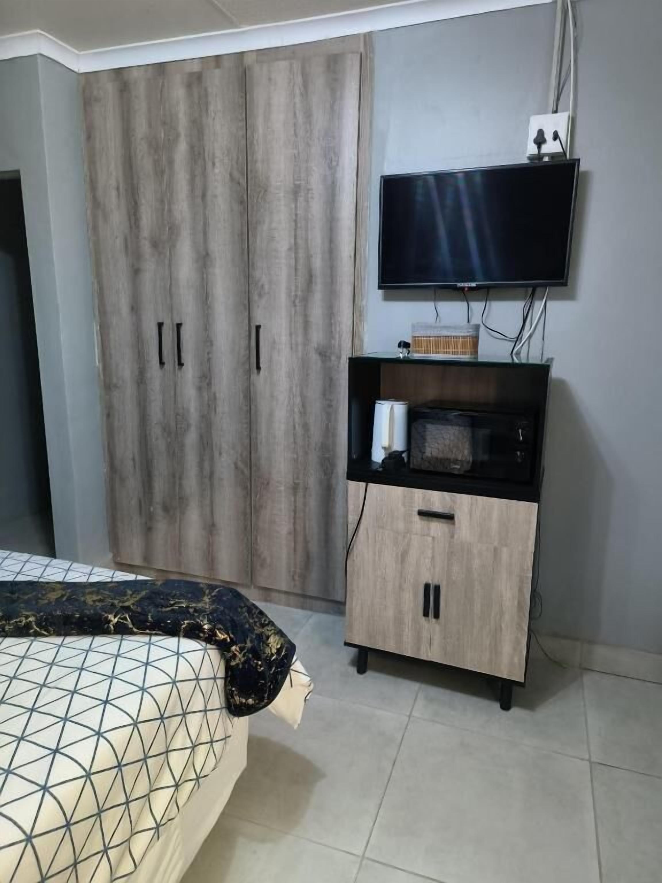 Un dormitorio con cama, armario, televisor y un mueble pequeño.