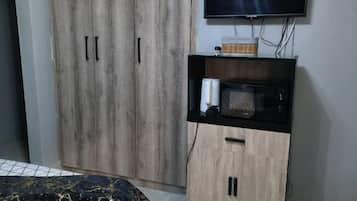 Un dormitorio con cama, armario, televisor y un mueble pequeño.
