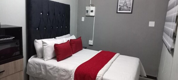 A hotel room with a bed, a bedside table, a wall-mounted power outlet, and a framed picture on the wall.