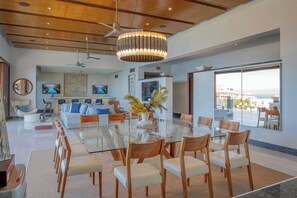 A modern dining area with a glass table, wooden chairs, and a ceiling fan. - 2 Villas, Luxury Amenities & Fully Staffed Service (Cabo San Lucas)
