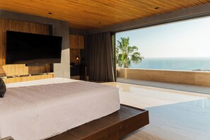 Een moderne slaapkamer met een groot bed, een flatscreen-tv en een balkon met uitzicht op de oceaan.