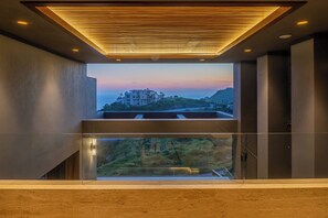 Een modern interieur met een groot raam met uitzicht op een kustlandschap in de zonsondergang.