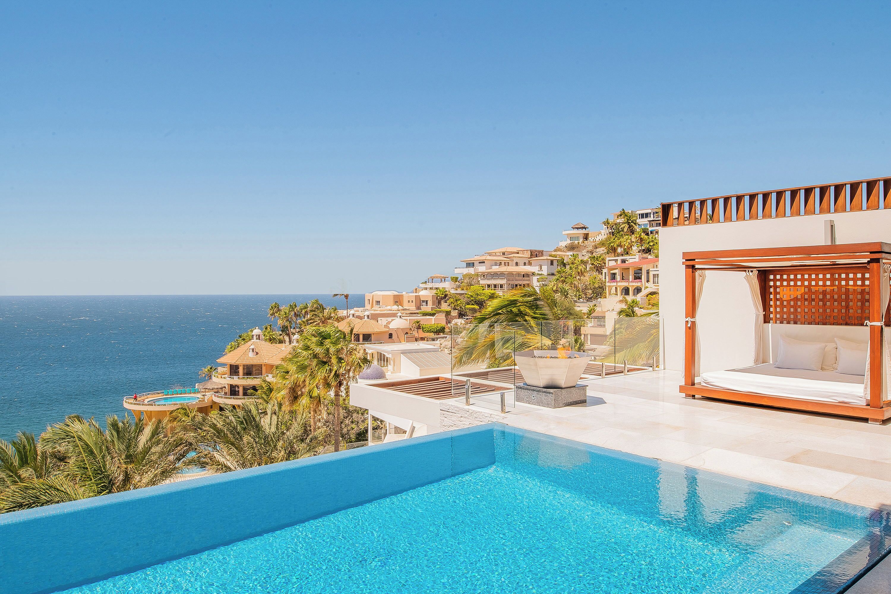 A pool with a view of the ocean, a wooden pergola, and a building with multiple balconies.