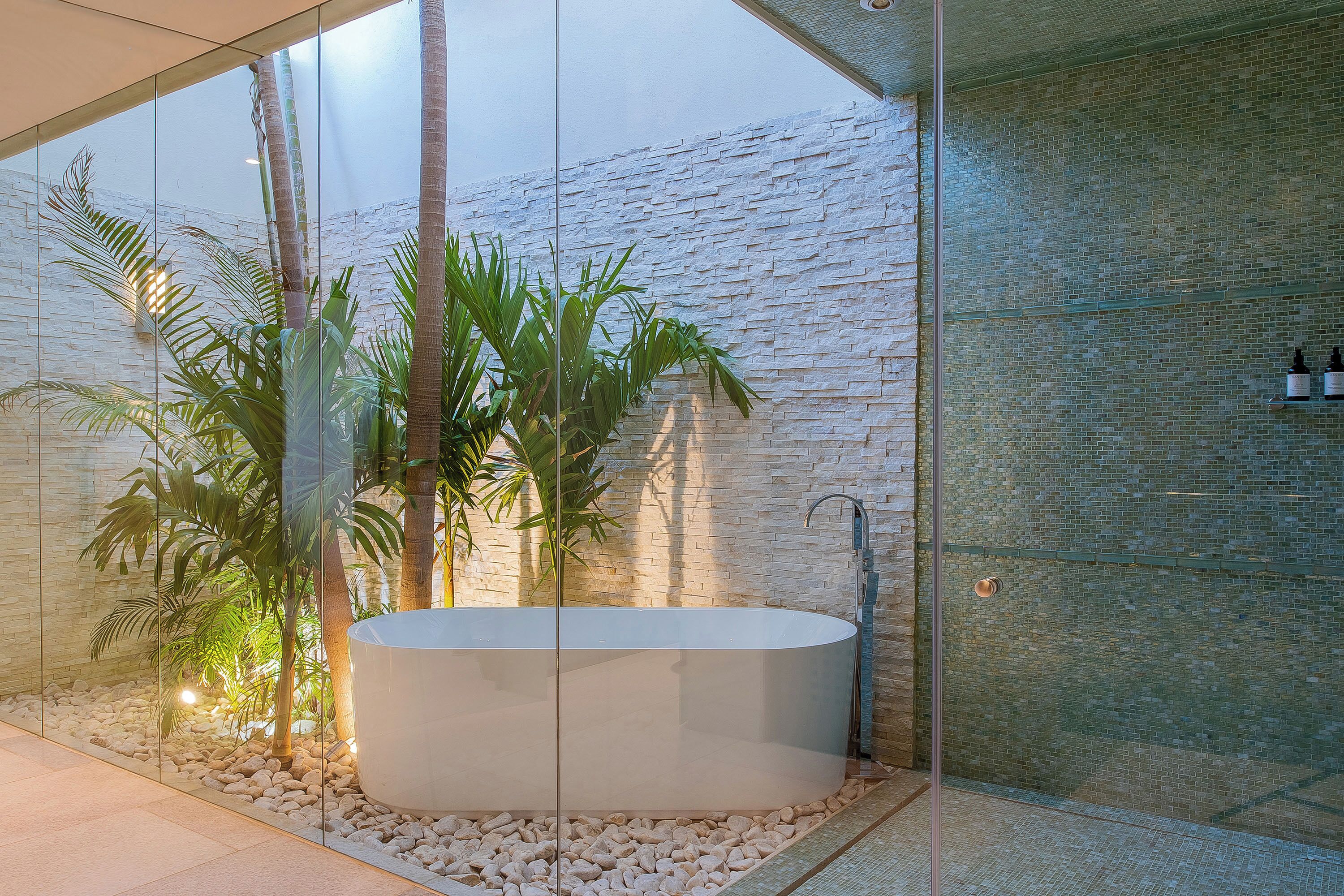 A modern bathroom with a freestanding bathtub, a glass-enclosed shower area, and a stone wall.