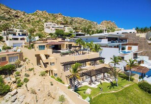 A residential area with multiple buildings, a swimming pool, and a hillside backdrop. - Luxury Pedregal Villa Pairing with Stunning Ocean Views (Cabo San Lucas)