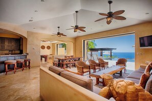 Un'ampia zona giorno con un divano grande, un tavolo da pranzo e sedie, una cucina con sgabelli da bar e vista sull'oceano.