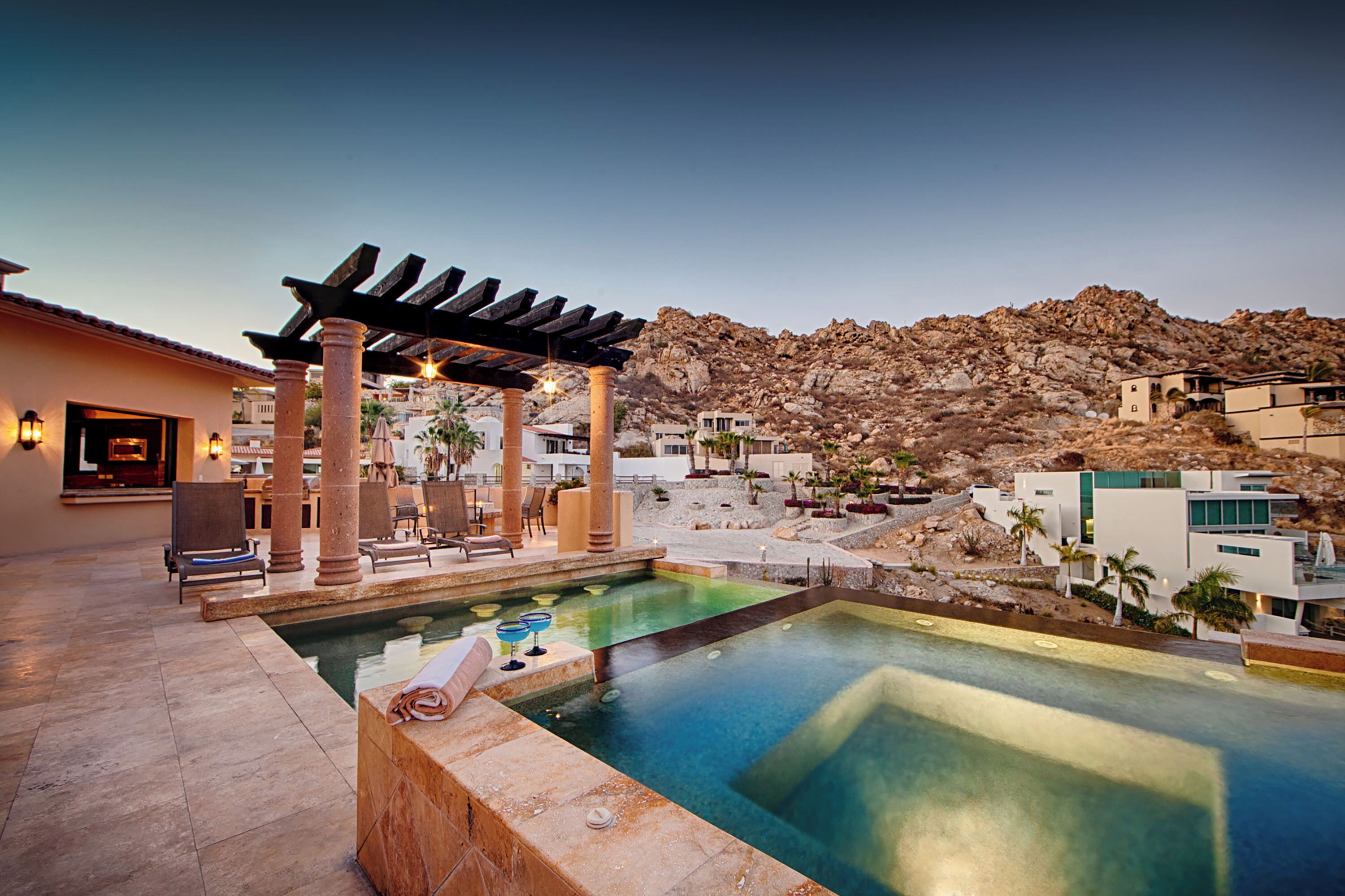A pool area with a pergola, lounge chairs, and a mountainous backdrop.