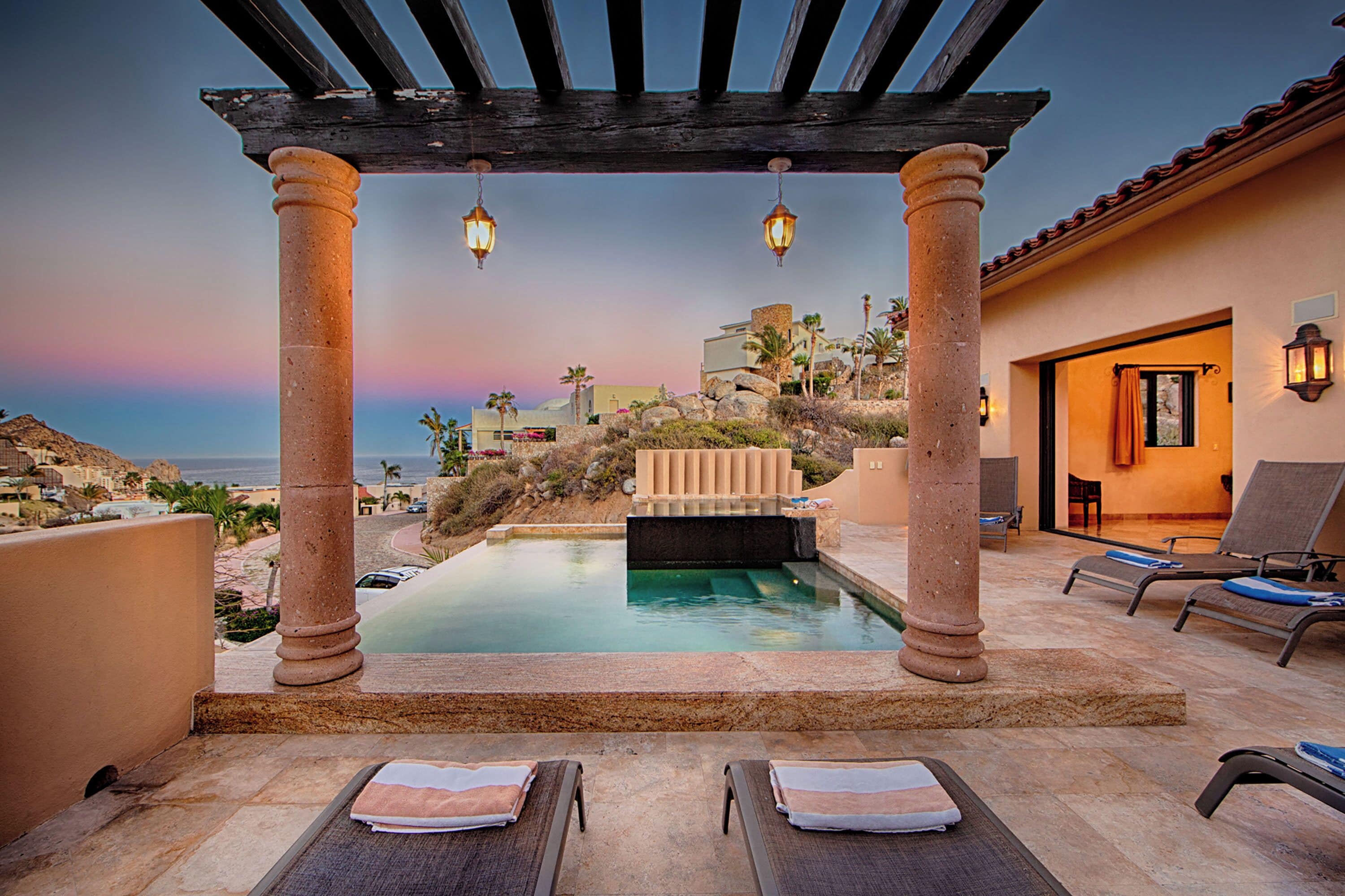A pool area with lounge chairs, a pergola, and a view of the surrounding landscape.