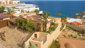 Ein Küstenwohngebiet mit Häusern mit Terrakotta-Dächern, Palmen und Blick auf das Meer.
