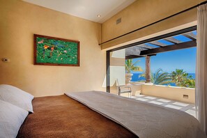 A bedroom with a bed, a painting, and a balcony with a view of the ocean. - Luxury Pedregal Villa Pairing with Stunning Ocean Views (Cabo San Lucas)