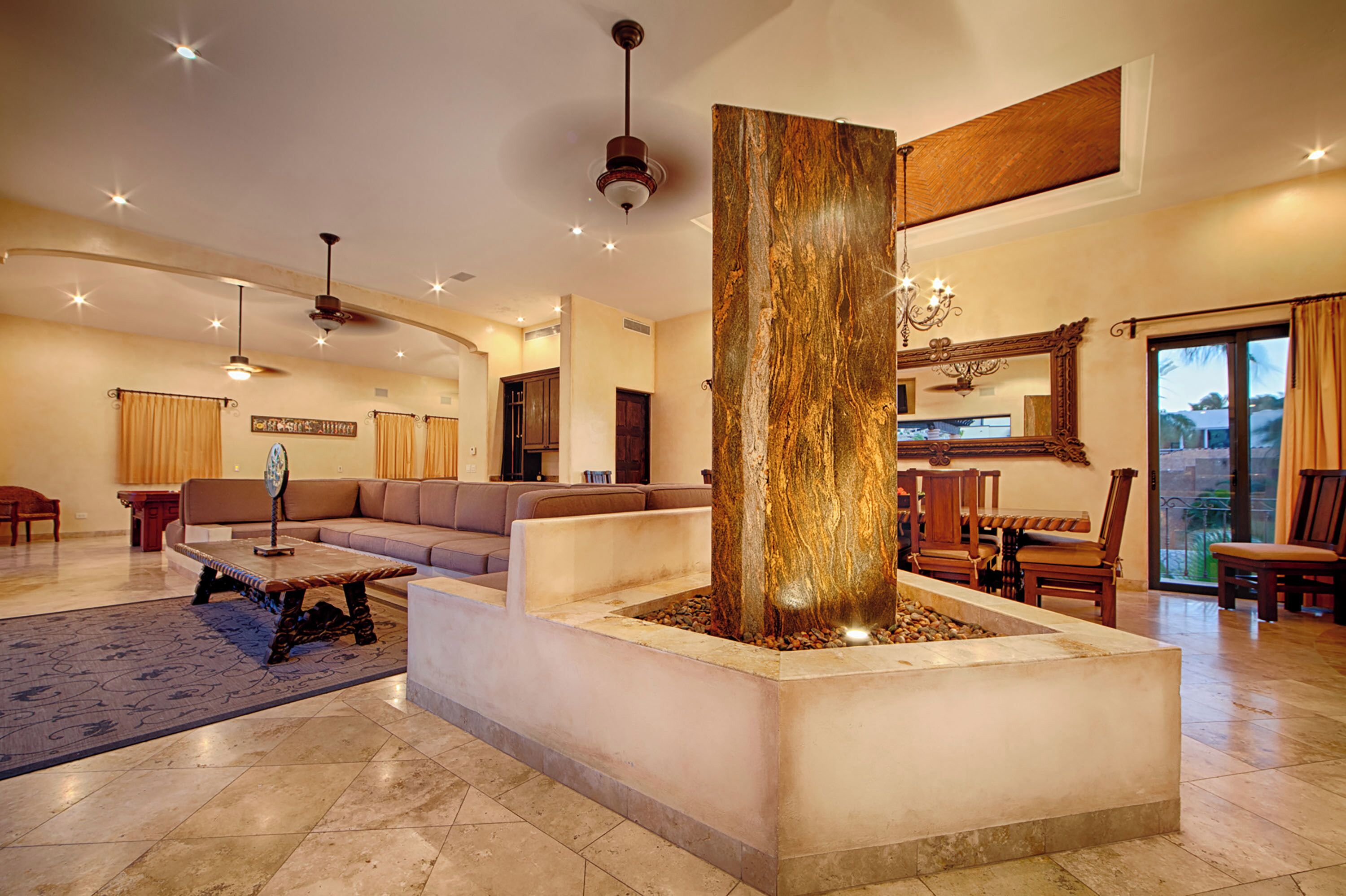 A spacious living area with a central column, a sofa set, a dining table with chairs, and a chandelier.