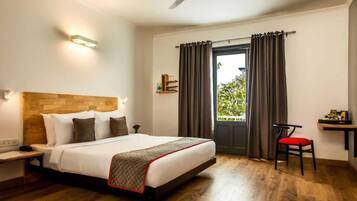 A hotel room with a bed, a desk, a chair, a ceiling fan, and a window with curtains.
