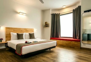 Hotellihuone, jossa on sänky, puinen pääty, yöpöydät, ikkuna verhoilla ja peili.