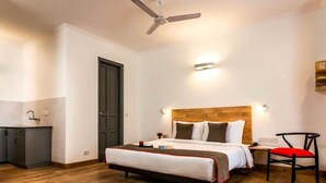 Een hotelkamer met een bed, een bureau, een stoel, een plafondventilator en een houten vloer.