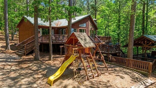 Eine Holzhütte mit Rutsche und Terrasse, umgeben von Bäumen.