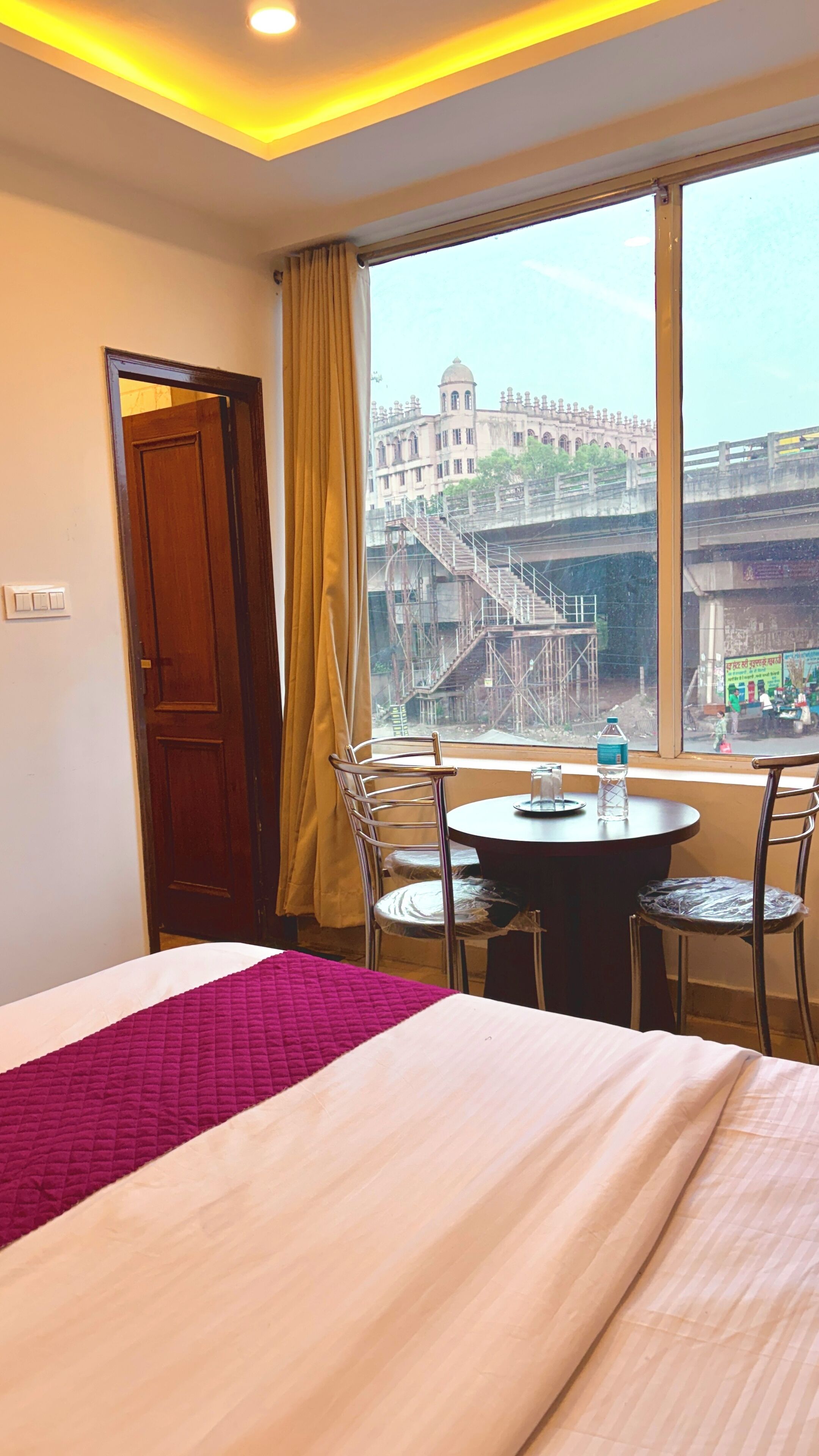 Habitación de hotel con cama, una mesa con sillas, ventana que ofrece vista a un edificio y un puente, y cortina.