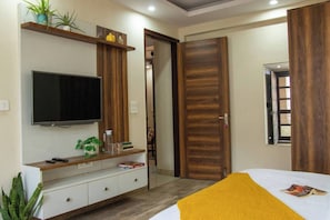 A bedroom with a bed, a TV mounted on the wall, a wooden door, and a window. - 401 - Designer Studio w/ Balcony - Golf Course Rd (Gurugram)