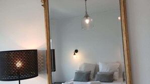 Une pièce dotée d’un grand miroir décoratif, d’un lit avec une literie blanche, d’une lampe fixée au mur et d’un luminaire au plafond.