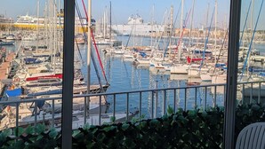 Une vue depuis un balcon donnant sur une marina, avec de nombreux bateaux et un grand navire en arrière-plan.