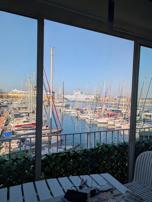 Blick von einem Balkon auf einen Yachthafen mit zahlreichen Booten und einem großen Schiff im Hintergrund.
