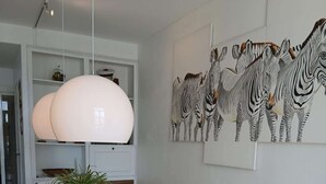 Un coin repas avec une table en verre, des chaises blanches, un grand luminaire suspendu et une décoration murale sur le thème des zèbres.