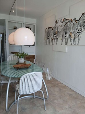 Ein Essbereich mit Glastisch, weißen Stühlen, einer großen Pendelleuchte und Wandkunst mit ZEBRA-Motiv.