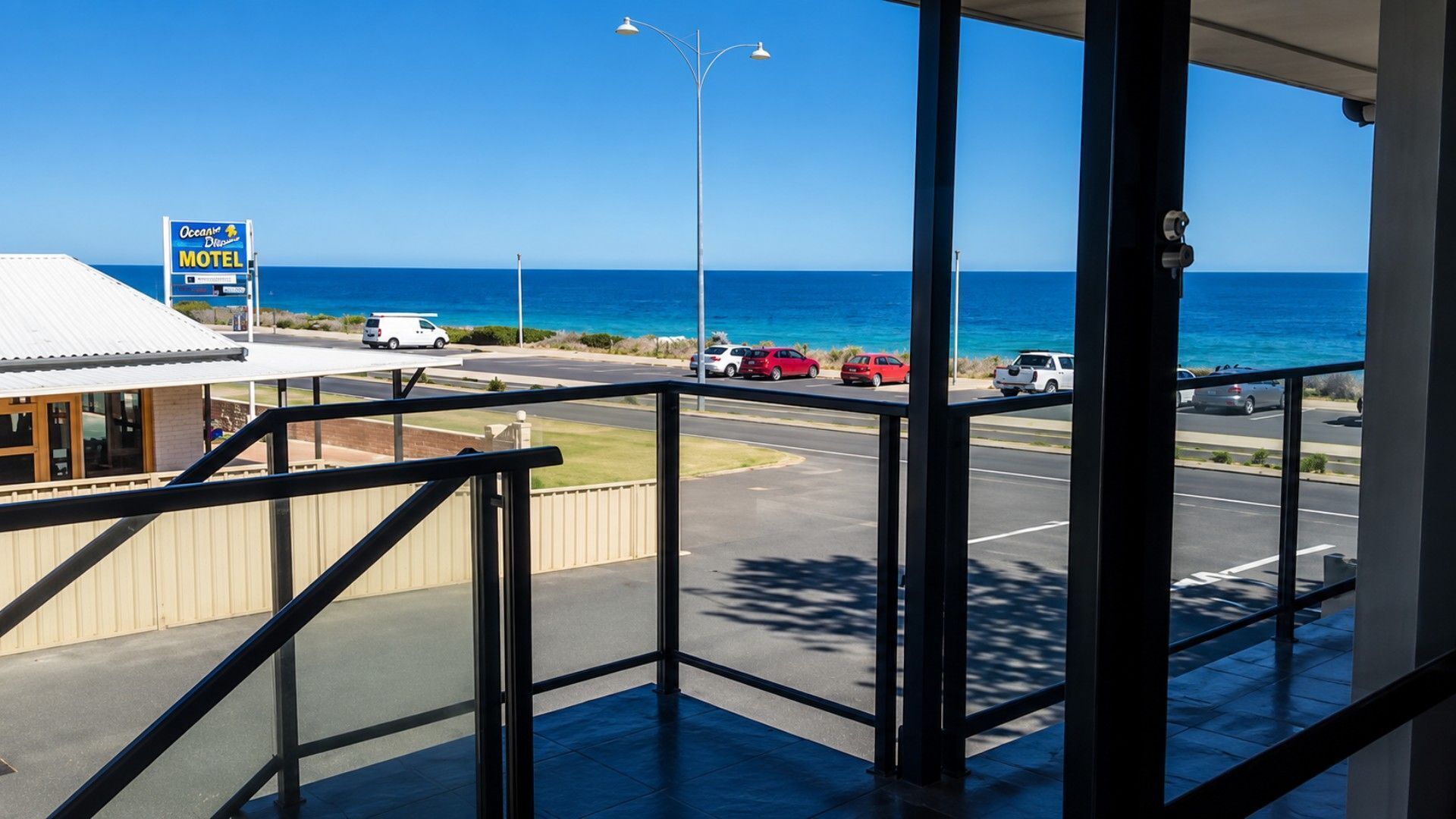 A motel with a view of the ocean, a parking lot with several cars, and a street lamp.