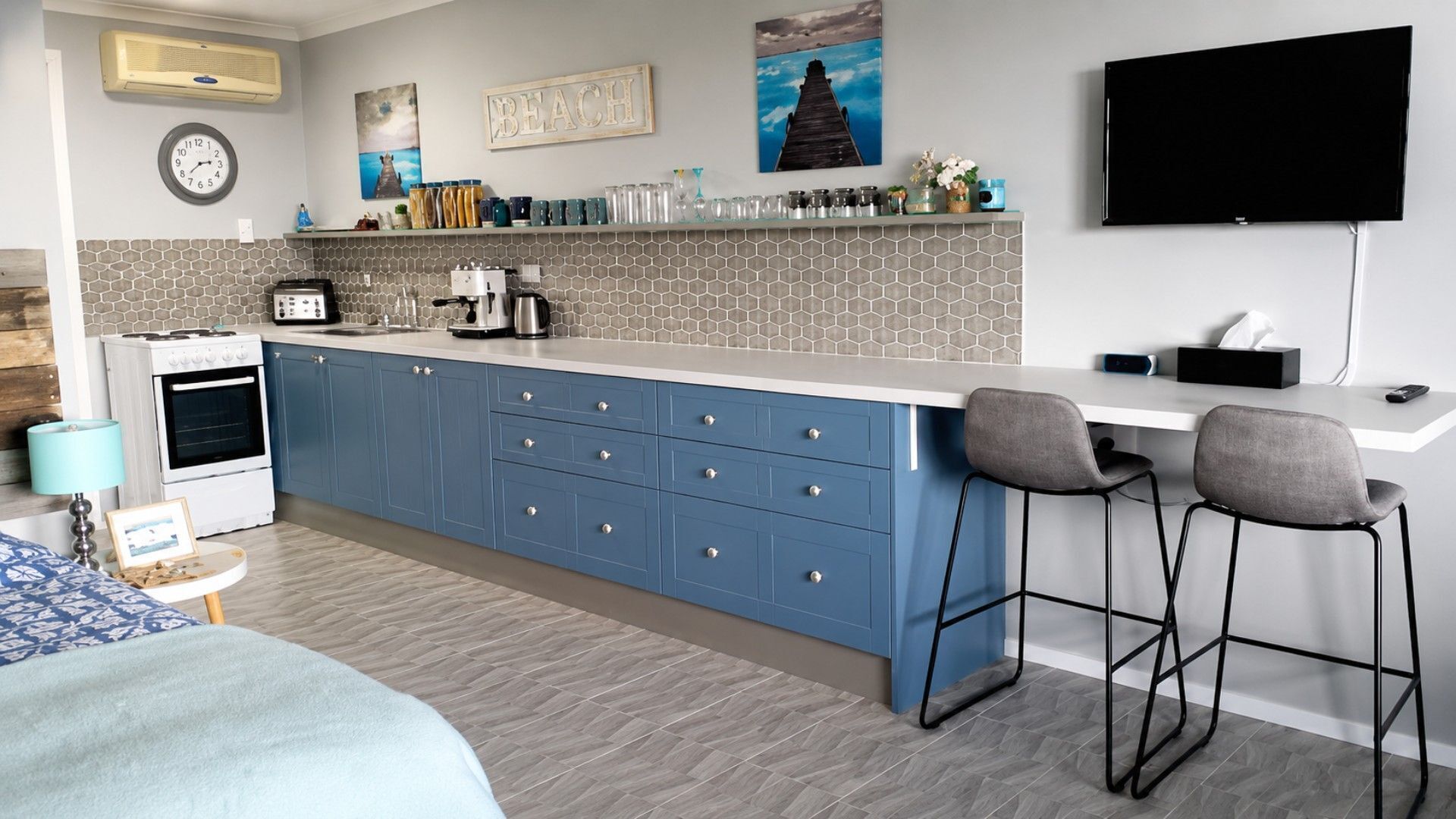 A modern kitchen with a central island, bar stools, a flat-screen TV, and a clock on the wall.