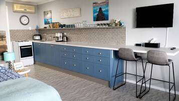 A modern kitchen with a central island, bar stools, a flat-screen TV, and a clock on the wall.