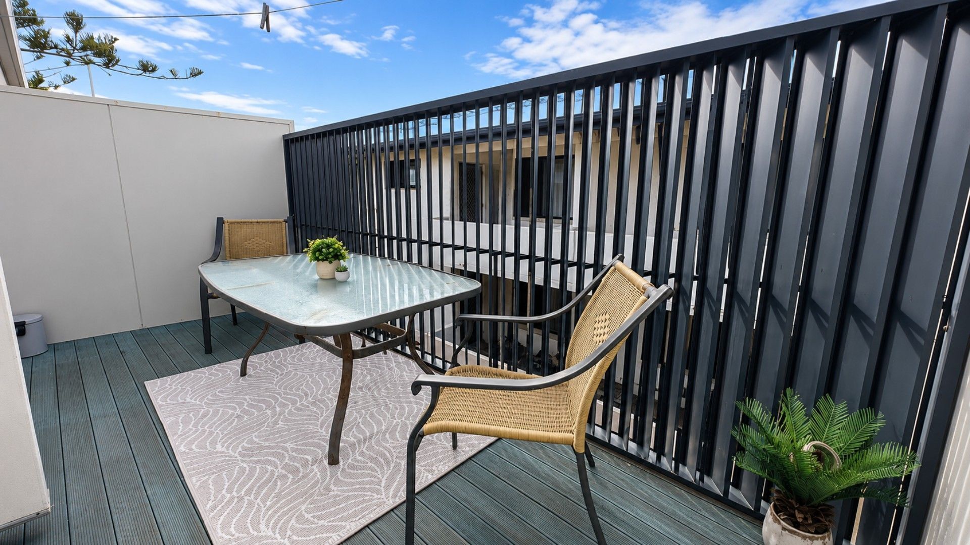 A patio with a table and chairs, a woven chair, a potted plant, and a metal fence.