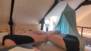 Et hyggeligt soveværelse med to senge, en himmelsseng og et lille bord med en lampe.