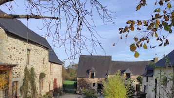 Une cour bordée de bâtiments en pierre, avec une terrasse en bois et un petit étang.