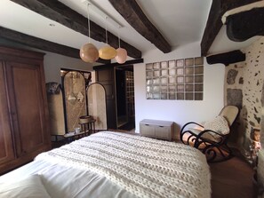Un dormitorio acogedor con una cama grande, vigas de madera, un cabecero tejido y una pared de piedra.