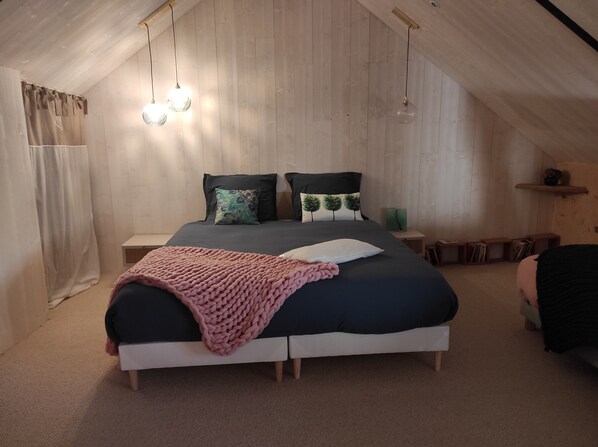A bedroom with a sloped ceiling, a bed with a pink blanket, two bedside tables, and a nightstand with a lamp.