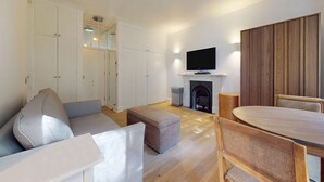 A modern living room with a sofa, ottoman, wooden dining table, and chairs. - Bright 1BR Kensington Flat-8 min Walk to Tube (London)
