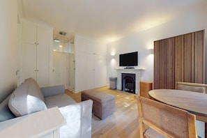 A modern living room with a sofa, ottoman, wooden dining table, and chairs. - Bright 1BR Kensington Flat-8 min Walk to Tube (London)