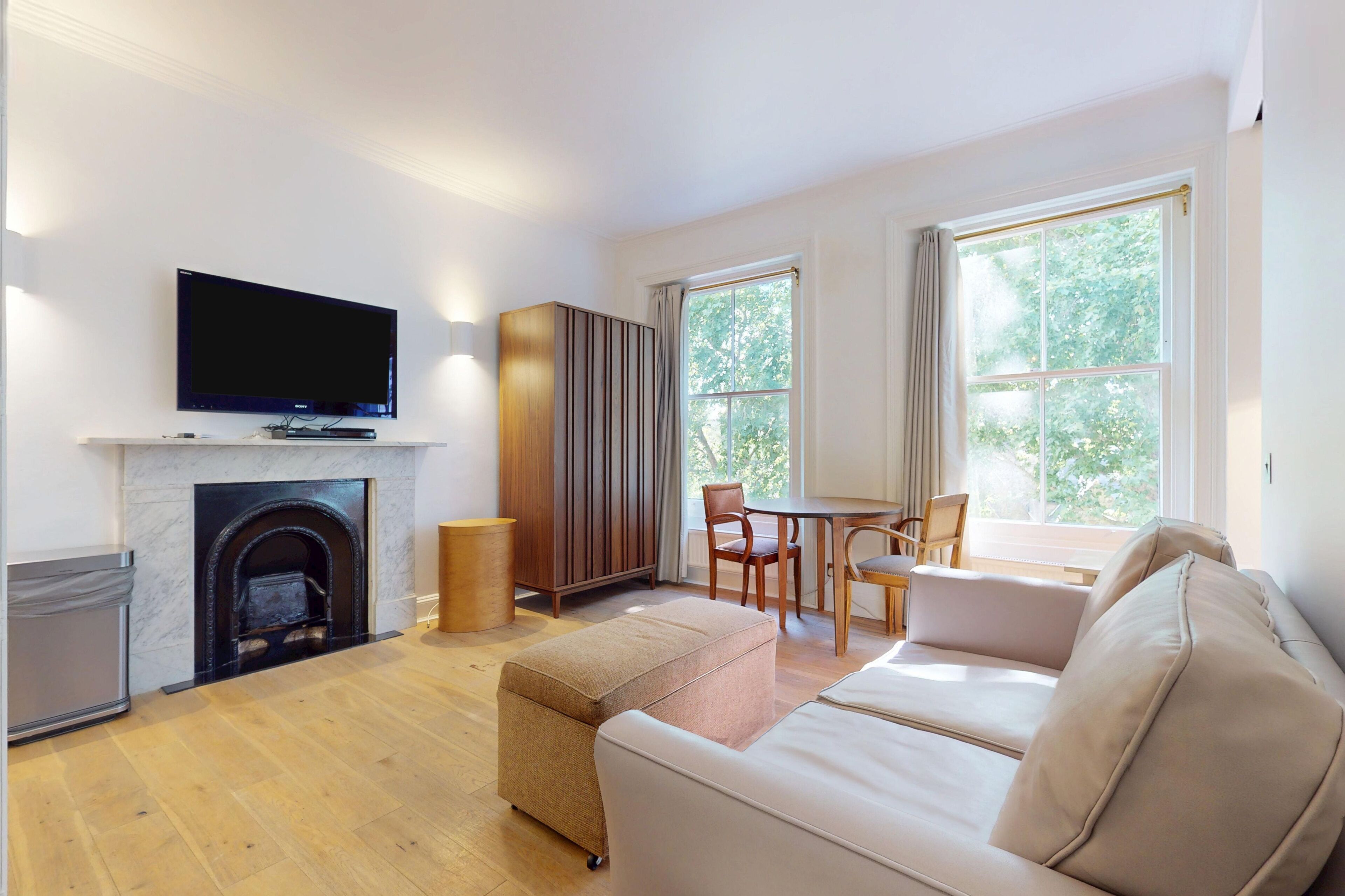 Una sala de estar con televisión de pantalla plana, chimenea, sofá, mesa de comedor con sillas y ventanas grandes.