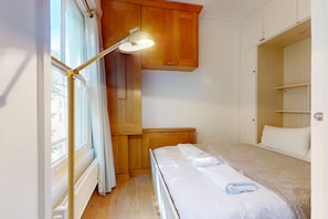 A room with a bed, a bedside table, a lamp, a wardrobe, and a window with curtains. - Bright 1BR Kensington Flat-8 min Walk to Tube (London)